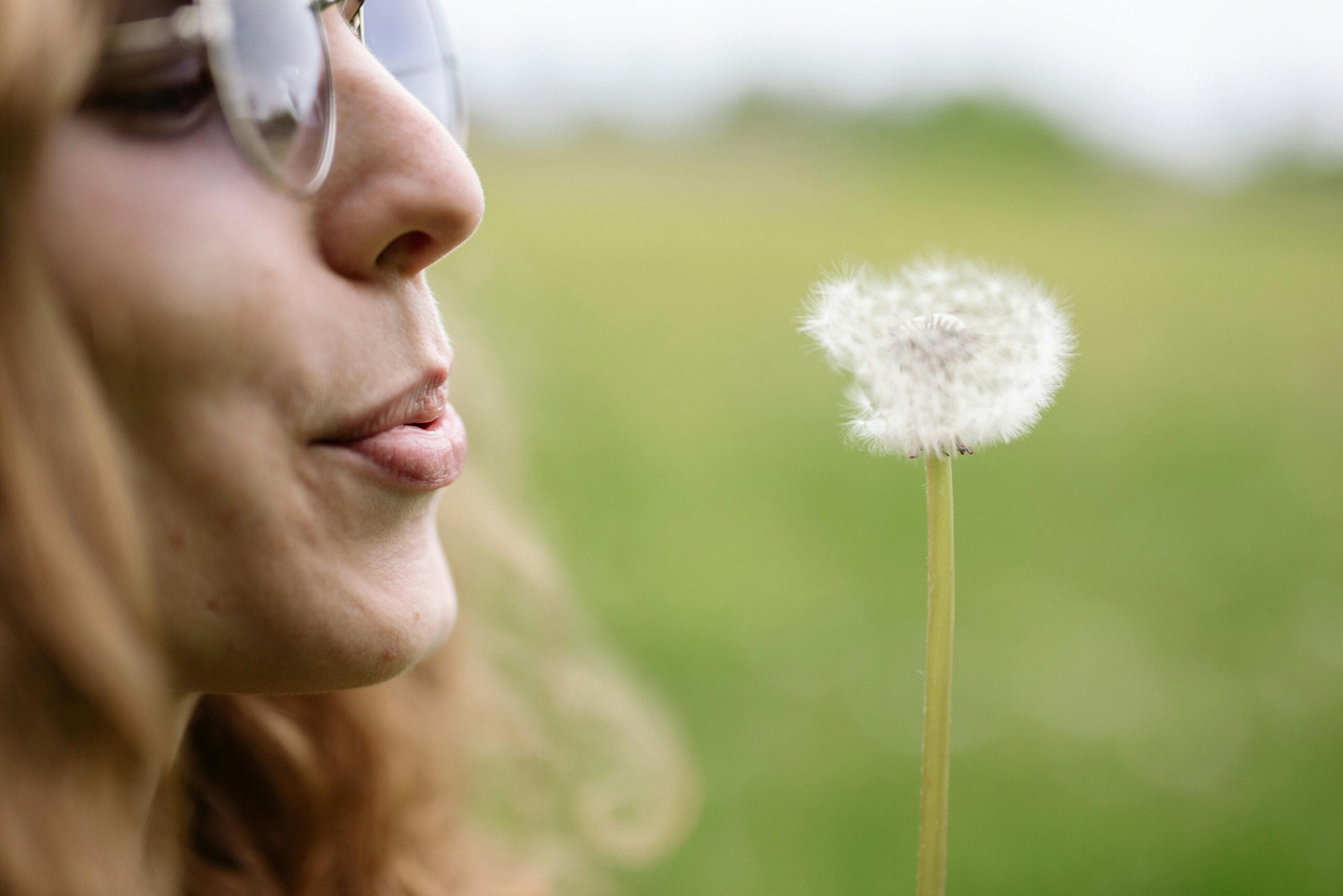 Tigard, OR, woman with fresh breath blowing away a dandelion after visiting a dentist near me
